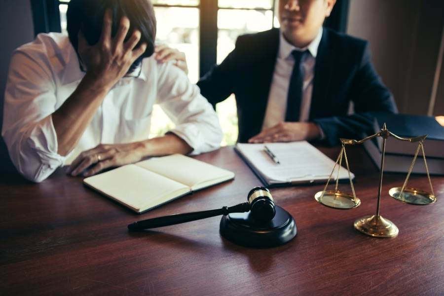 Lawyer consoling distressed client during legal consultation with gavel and justice scales on desk