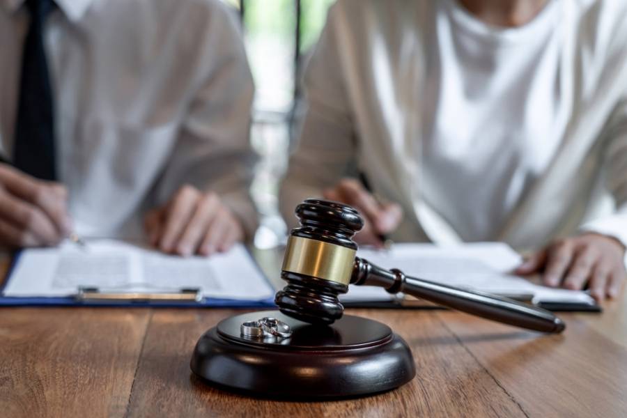 Close-up of gavel with wedding rings in front of couple signing legal divorce documents