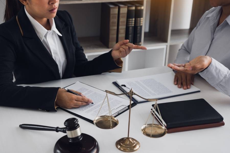 Female lawyer consulting with client over legal documents with gavel and justice scales on desk