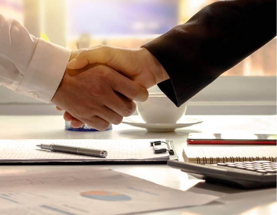 Close-up of a handshake between two professionals over contract paperwork and financial documents, symbolizing successful timeshare cancellation agreements with TimeshareBeGone in Maine.