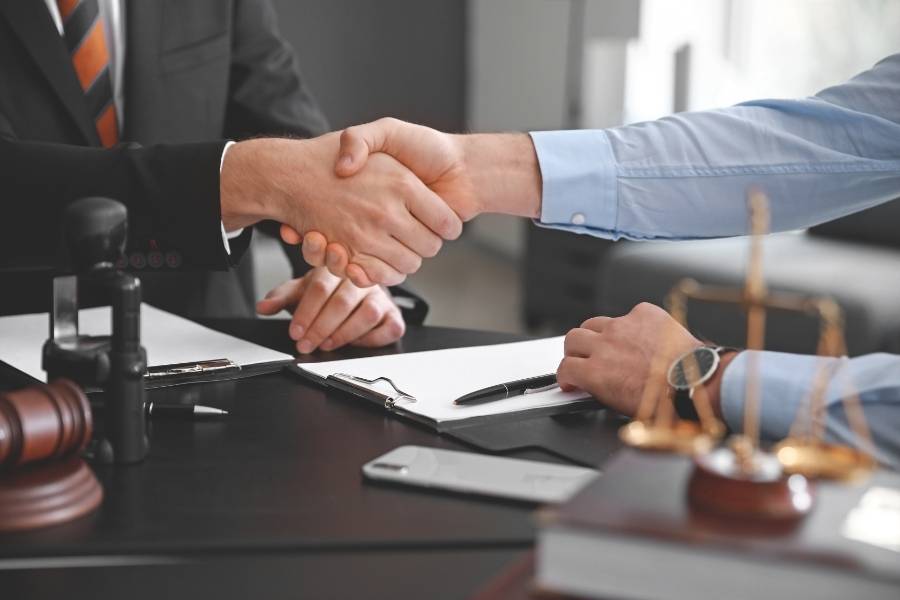 Lawyer and client shaking hands after successful legal agreement with gavel and justice scales on desk