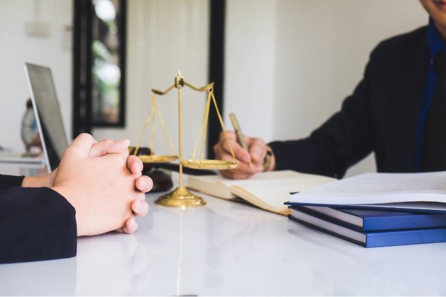 Lawyer taking notes during legal consultation with client, justice scales and law books on desk