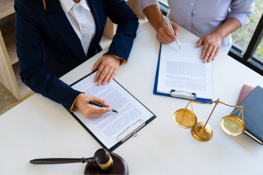 Lawyer and client signing legal documents with gavel and justice scales on desk