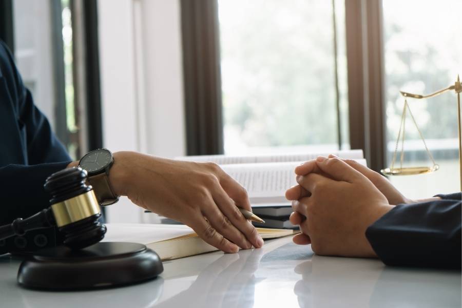 Lawyer pointing at legal document during consultation with client, gavel and justice scales on desk
