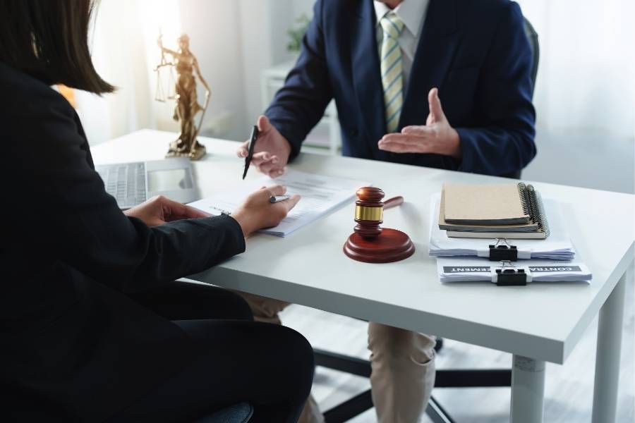 Lawyer discussing legal agreement with client in office, gavel and Lady Justice statue on desk