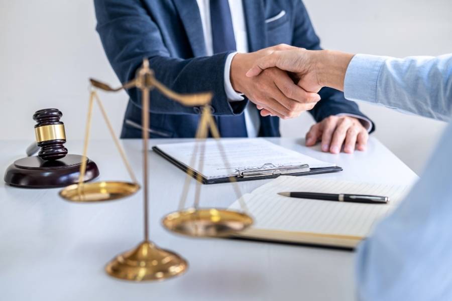 Attorney shaking hands with client after successful legal agreement, with gavel, scales of justice, and signed contract in West Virginia.