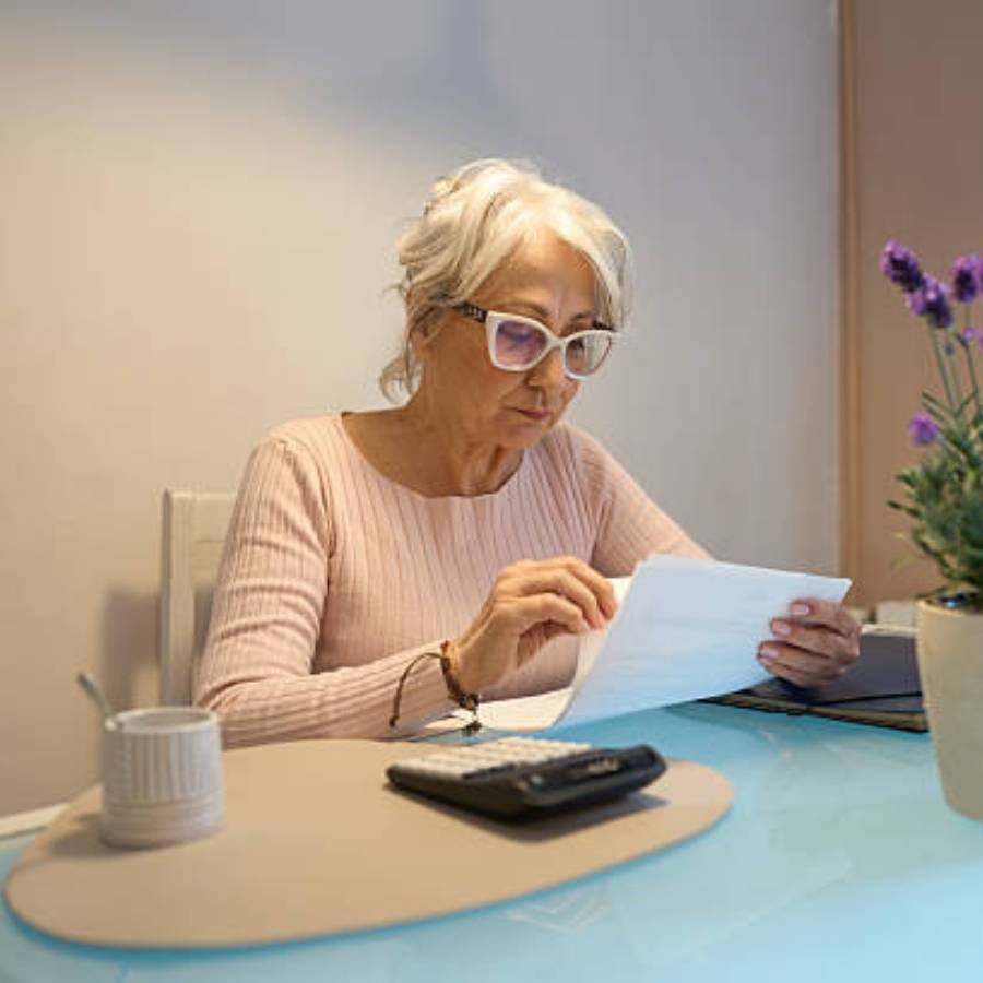 Senior woman reviewing timeshare cancellation paperwork in Pennsylvania at home with calculator on table.
