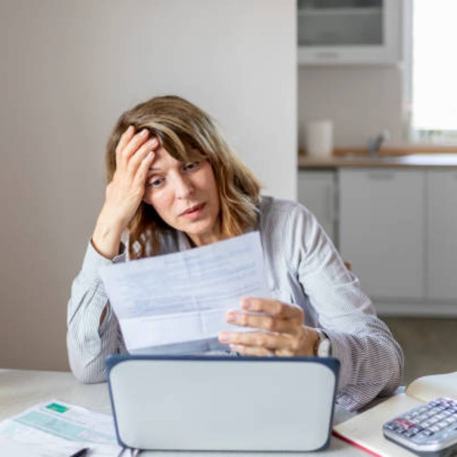 Frustrated woman reviewing timeshare cancellation documents in Rhode Island while sitting at home with laptop and calculator.