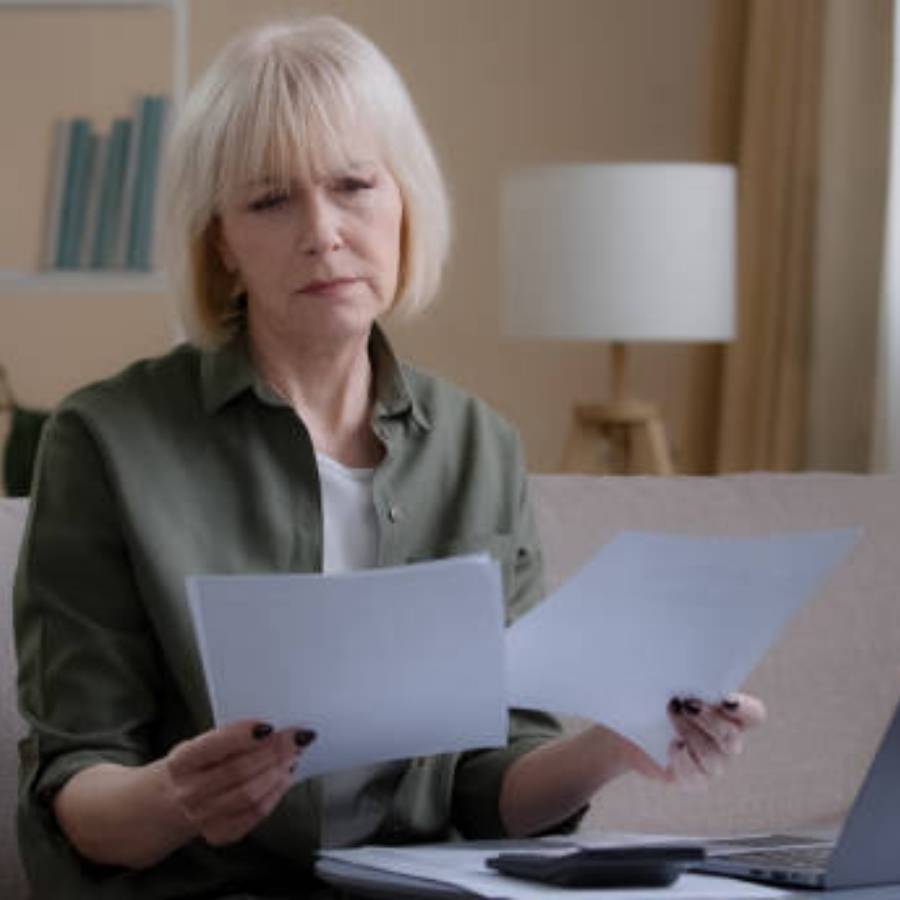 Serious senior woman reviewing timeshare cancellation documents at home in South Dakota, with laptop and calculator on table