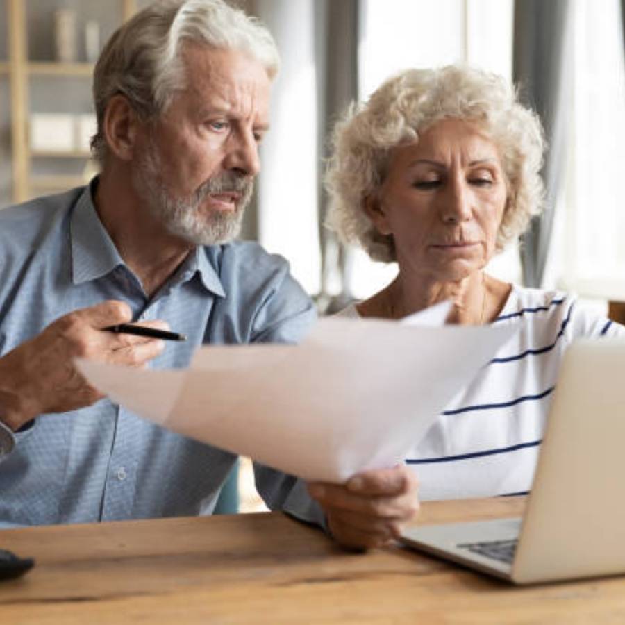 Senior couple reviewing documents and researching timeshare cancellation in Vermont on a laptop.