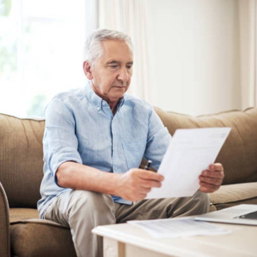 Older man sitting on couch reviewing timeshare cancellation paperwork with pen in hand in Wisconsin